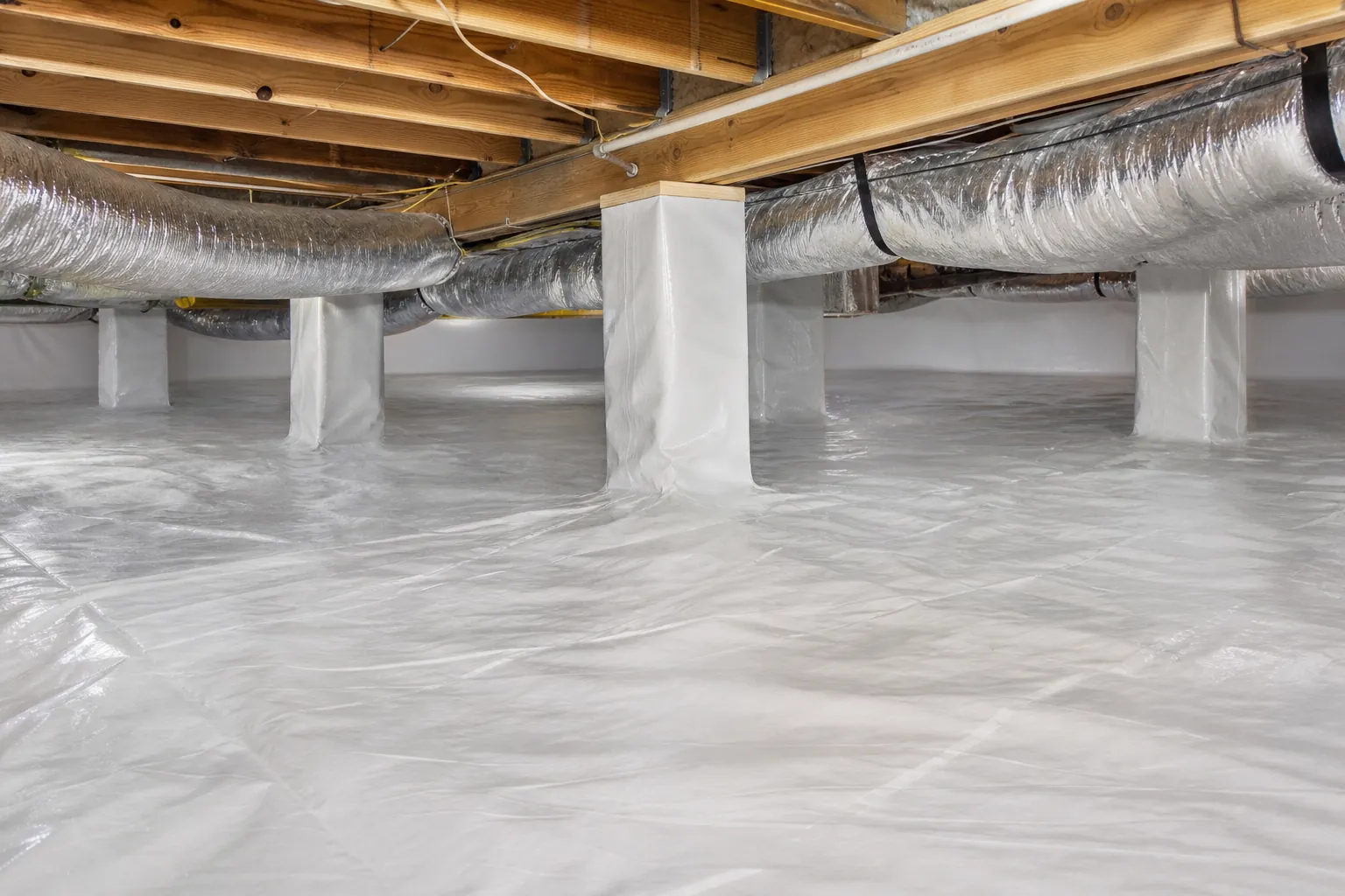 Encapsulated crawl space with white vapor barrier covering the floor and support piers beneath wooden joists and silver ductwork.