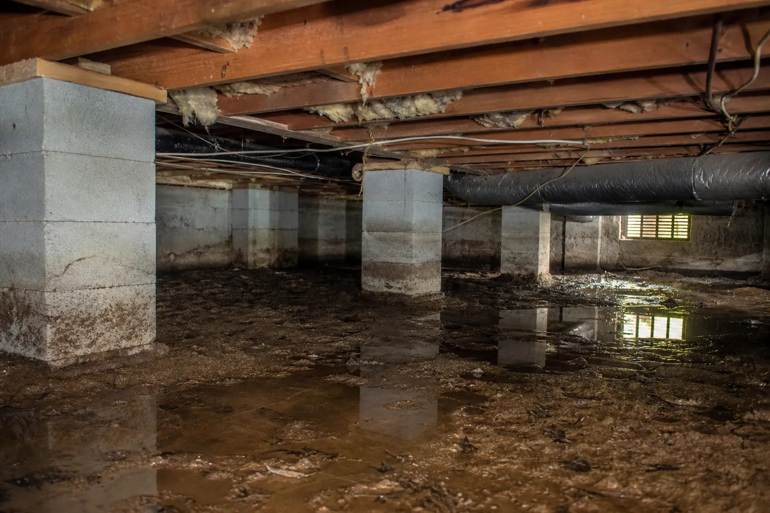 Wet, muddy crawl space with standing water, concrete piers, exposed floor joists, insulation, and HVAC ductwork