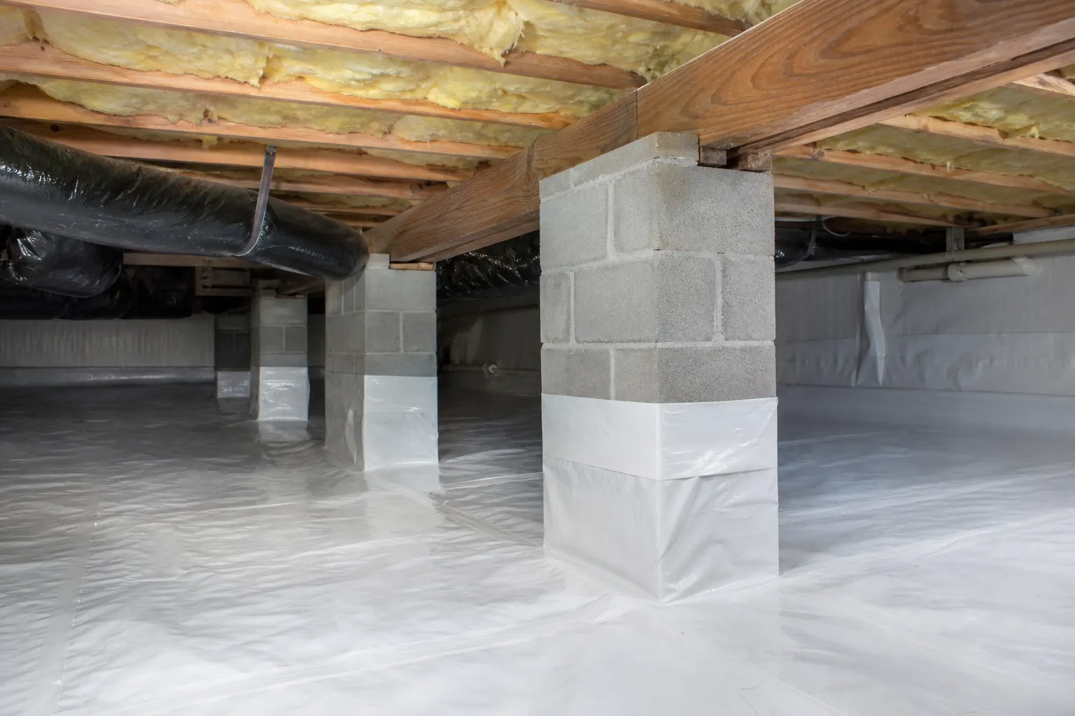 Encapsulated crawl space with white vapor barrier sealed around concrete block piers beneath insulated floor joists.