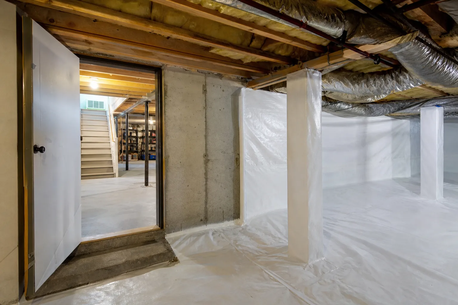 White vapor barrier encapsulates a crawl space beside an open doorway leading into a concrete basement.