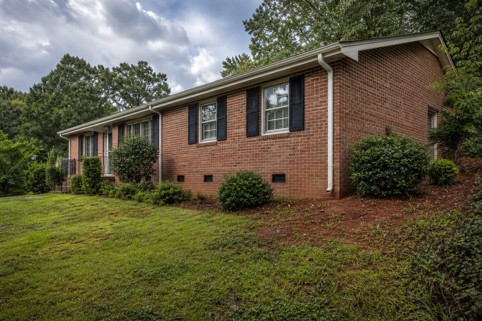 Older brick ranch with crawl space vents on a rolling red-clay lot after rain
